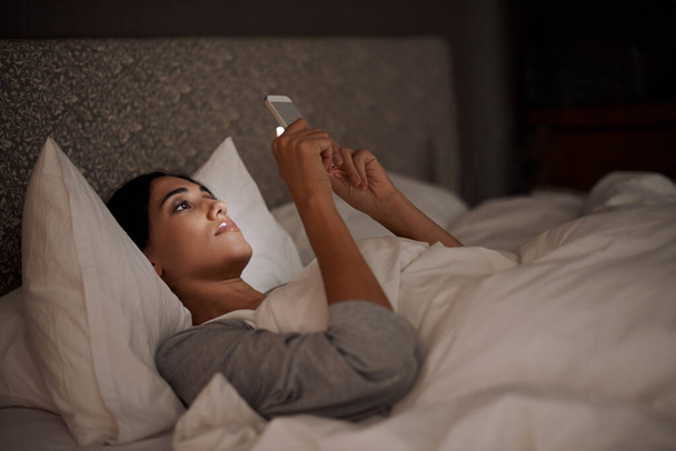 Saying goodnight to my love. A young woman sending a text message while in bed - Foto, afbeelding