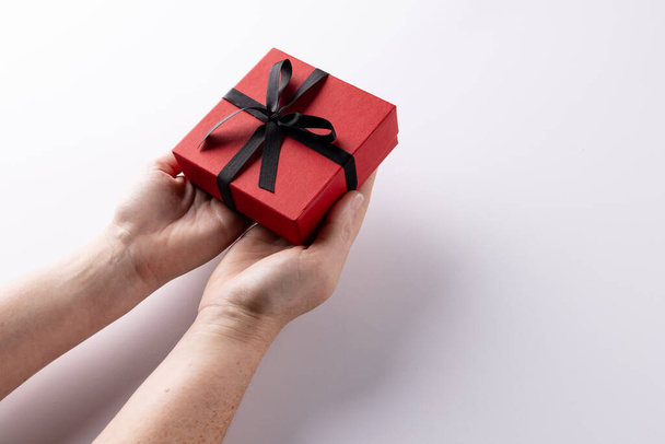 Hands holding red gift box tied with black ribbon, on white background with copy space. Valentine's day, birthday, love, romance and celebration concept. - Valokuva, kuva