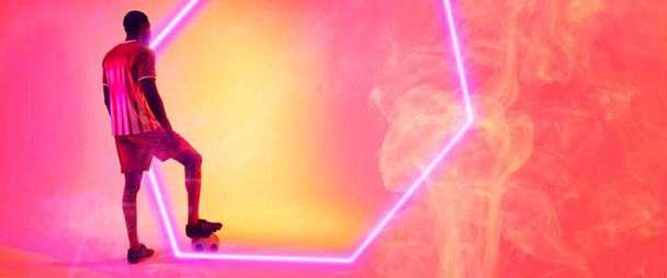 Un footballeur afro-américain debout près de l'hexagone illuminé sur fond fumé. Espace de copie, composite, sport, soccer, compétition, néon, illustration, lumineux et abstrait. - Photo, image