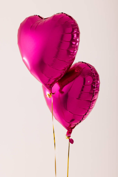 Vertical of two shiny pink heart shaped balloons floating on white background with copy space. Valentine's day, love, romance and celebration concept. - Foto, afbeelding