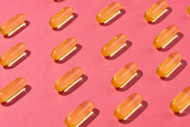 Composition of oil capsules arranged in rows on pink background. Medicine, medical services, healthcare and health awareness concept. - 写真・画像