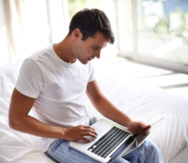 Sprawdzam jego maile w AM. przystojny młody mężczyzna korzystający z laptopa na skraju łóżka - Zdjęcie, obraz