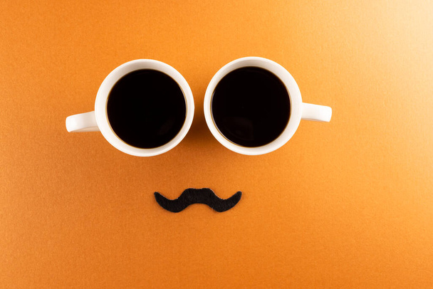Composition of fake moustache and cups of coffee on orange background with copy space. Fake moustache day, party, celebration and costume concept. - Φωτογραφία, εικόνα