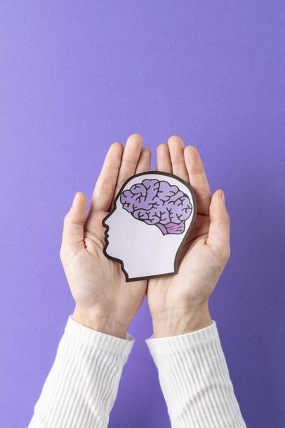 Composition of hands holding head silhouette with brain on purple background. Medicine, healthcare, science and copy space concept, digital composite image. - Zdjęcie, obraz