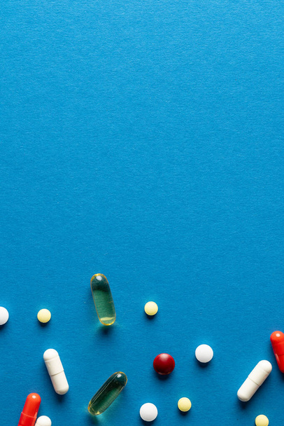 Vertical composition of a variety of pills and capsules on blue background with copy space. Medical services, medicine, healthcare and health awareness concept. - Фото, изображение