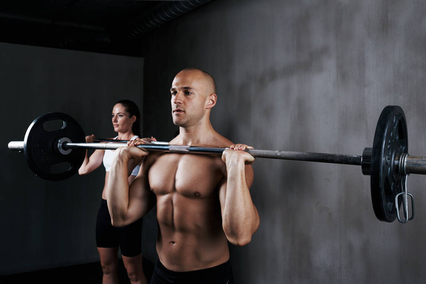 Training to become fighting fit. two people lifting barbells during a gym workout - Foto, Imagem