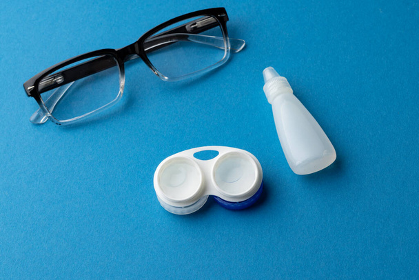 Composition of glasses with contact lenses case and eye drops and on blue background with copy space. Medical services, healthcare and health awareness concept. - Foto, immagini