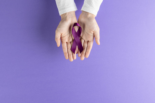 Hands holding purple pancreatic cancer awareness ribbon on purple background with copy space. Medical services, healthcare and health awareness concept. - Valokuva, kuva