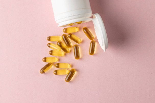 Composition of white pill box spilling oil capsules on pink background with copy space. Medicine, medical services, healthcare and health awareness concept. - 写真・画像