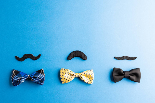 Composition of fake moustaches and bow ties on blue background with copy space. Fake moustache day, party, celebration and costume concept. - Valokuva, kuva