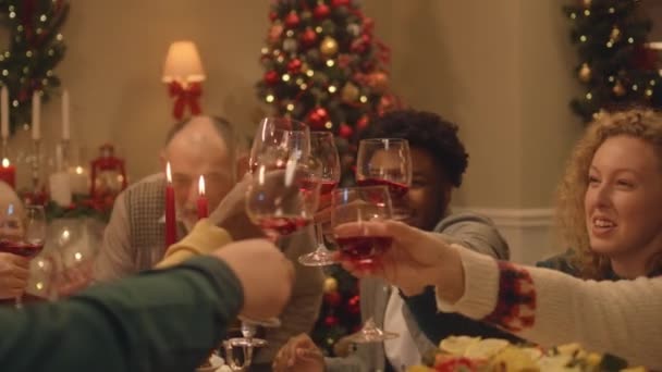 Gelukkige multiculturele familie vieren Kerstmis of Nieuwjaar, het opvoeden van wijnglazen. Geserveerd vakantietafel met verschillende gerechten en kaarsen. Warme sfeer van familie kerstdiner thuis. Proost.. - Video