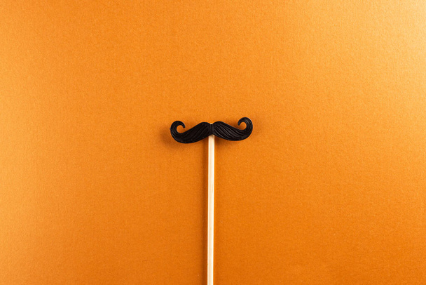 Composition of fake moustache on stick on orange background with copy space. Fake moustache day, party, celebration and costume concept. - Φωτογραφία, εικόνα