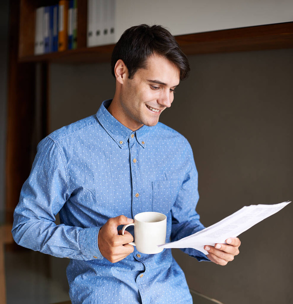 Proofreading a report. A young businessman holding a cup of coffee while going through some paperwork - Photo, Image