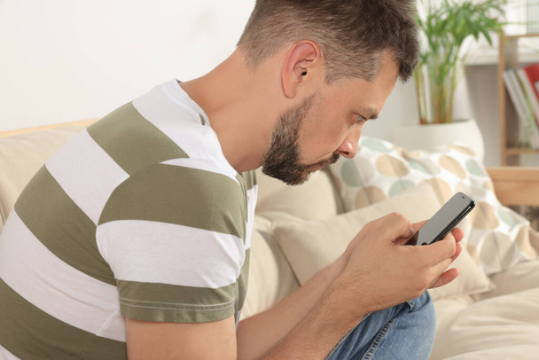 Man with poor posture using smartphone on sofa at home - Foto, Bild