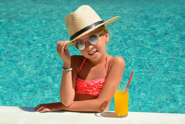 Cute little girl with glass of juice in swimming pool on sunny day - Foto, Imagen