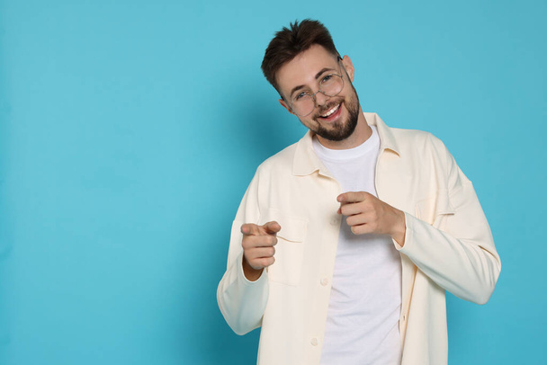 Handsome man in white jacket pointing fingers on light blue background, space for text - Φωτογραφία, εικόνα