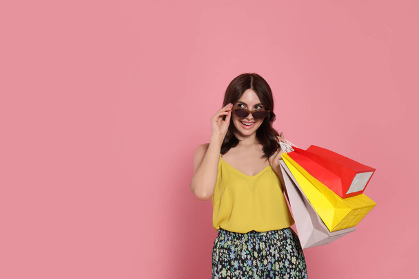 Beautiful young woman with paper shopping bags on pink background. Space for text - Foto, imagen
