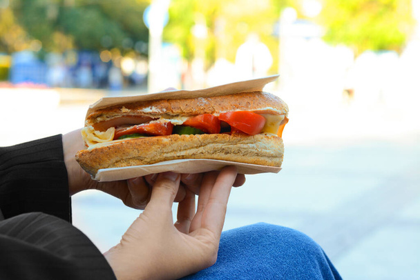 Woman holding tasty sandwich with vegetables outdoors, closeup. Street food - 写真・画像