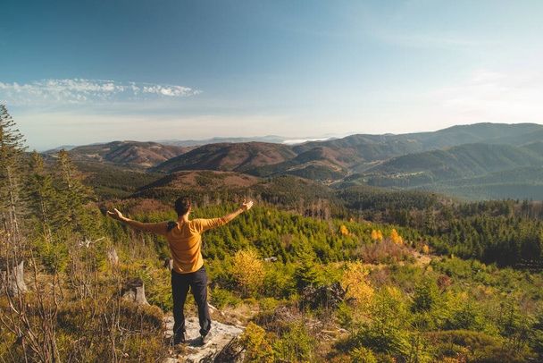 Enthusiastic traveller stands on a rock and looks down into the valley. Happy to have reached his goal. Pumping energy for the next journey. Horni Lomna, Beskydy mountains, Czech republic. - Fotografie, Obrázek