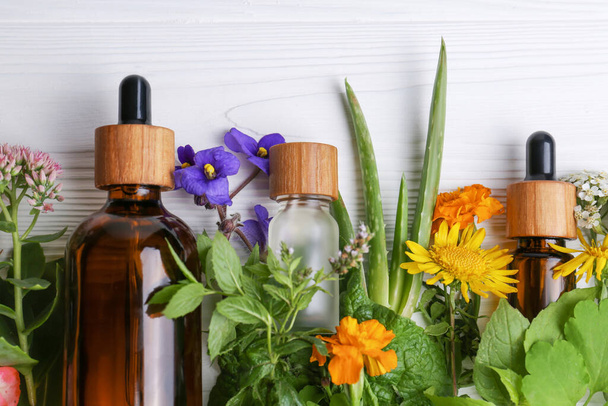 Glass bottles of aromatic essential oil and different wildflowers on white wooden table, flat lay. Space for text - Foto, afbeelding