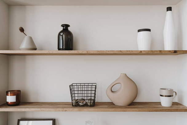 Decorated shelf on white wall. Aesthetic luxury minimalist home interior design decoration. Elegant Scandinavian, hygge style interior. Picture frames, fragrance, vase, books, candle - Fotó, kép