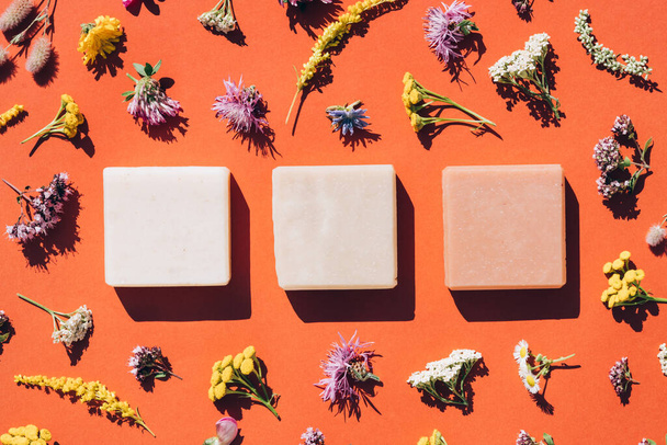 Handmade organic soap bars made with natural ingredients, flowers and herbs over orange background. Making herbal soap at home. View above, flat lay style - Photo, Image