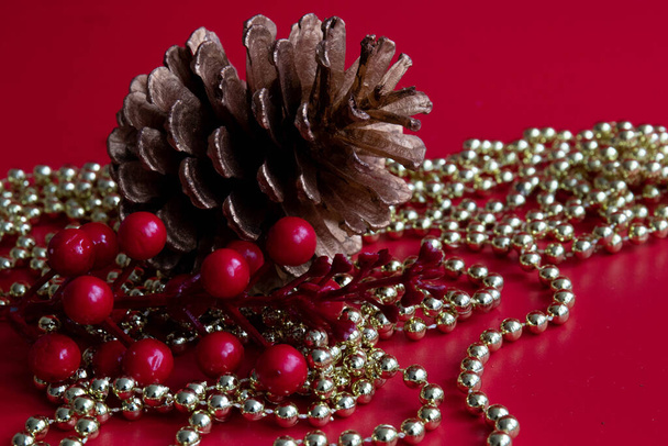 Pine Cone, red berries, gold chain, red background - Fotografie, Obrázek