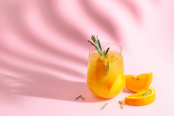 Summer cocktail with orange, rosemary, and ice. Drink on pink background with palm leaf shadow. Summer, tropical, fresh cocktail concept. - 写真・画像