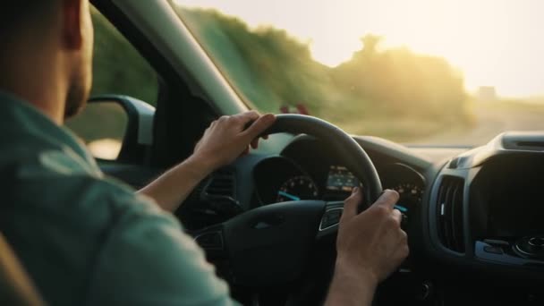 Az ember egy autót vezet az úton, a lenyugvó nap süt a szélvédőn. Kilátás a járművezetők válla mögül - Felvétel, videó
