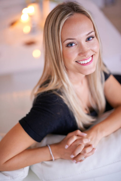 She has the most radiant smile. Portrait of a young blonde woman sitting on her sofa at home - Fotografie, Obrázek