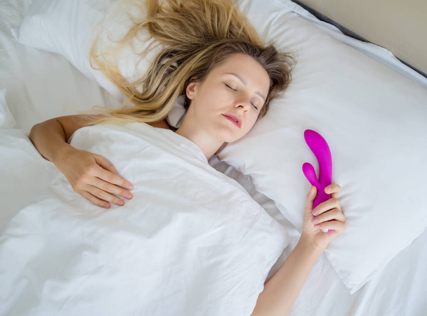 Young sexy woman in the bed holding in her hands a sex toy for adults. - Foto, Imagem
