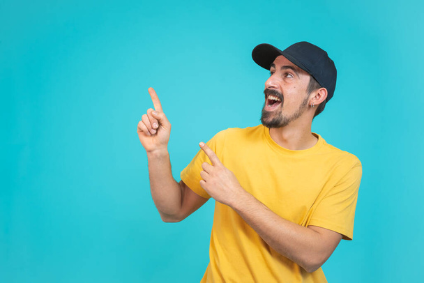 Surprised happy young bearded man in casual outfit pointing away with two hands and fingers over isolated background. Mock up Copy space shows good offers. High quality photo - Фото, изображение