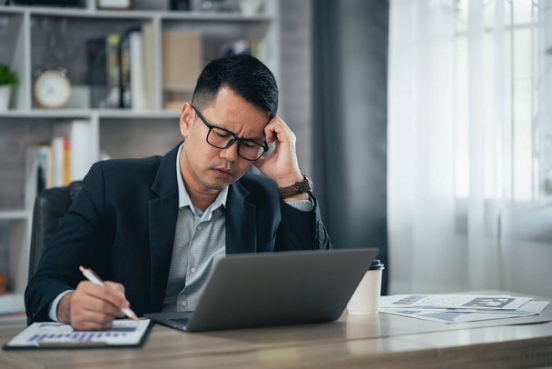 Ázsiai üzletember visel szemüveget, és kéz a kézben fej, amelynek stresszes depresszió szomorú idő, miközben dolgozik laptop otthon. Depressziós férfi szomorú sorozat dolgozik otthonról. Dolgozni bárhol koncepció. - Fotó, kép