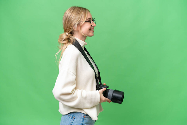 Jonge fotografe Engelse vrouw over geïsoleerde achtergrond in laterale positie - Foto, afbeelding