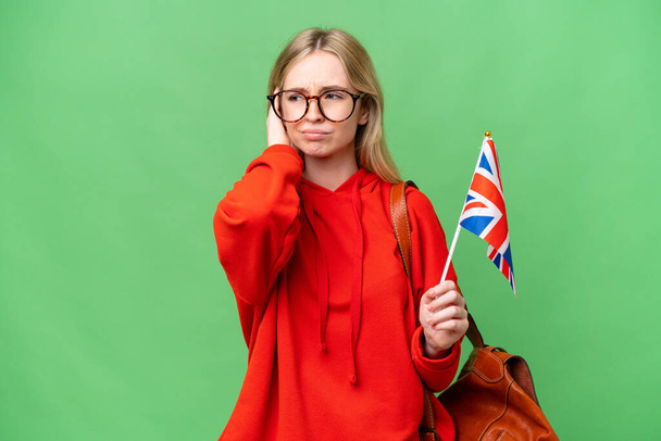 Молода жінка, що тримає прапор Сполученого Королівства над ізольованим фоном розчарована і покриває вуха. - Фото, зображення