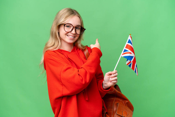 Junge hispanische Frau mit einer britischen Flagge vor isoliertem Hintergrund, die nach hinten zeigt - Foto, Bild