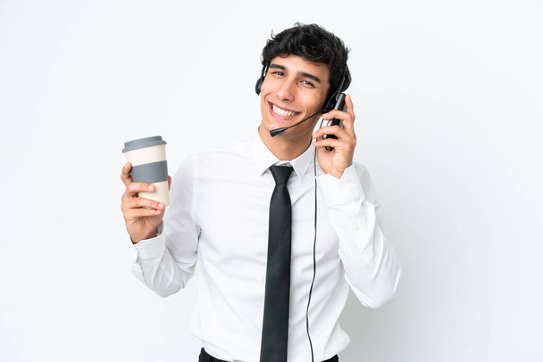 Hombre de telemarketer trabajando con un auricular aislado sobre fondo blanco sosteniendo café para llevar y un móvil - Foto, Imagen