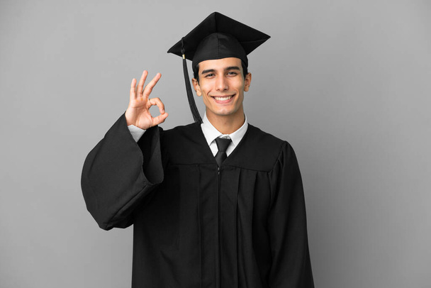 Fiatal argentin egyetemi diplomás elszigetelt szürke háttér mutatja rendben jel ujjakkal - Fotó, kép
