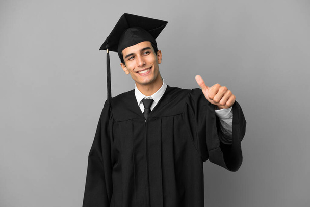 Νεαρός Αργεντινός απόφοιτος πανεπιστημίου απομονωμένος σε γκρίζο φόντο κάνοντας μια χειρονομία - Φωτογραφία, εικόνα