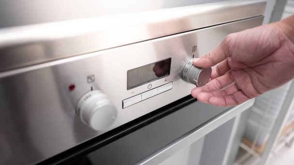 キッチンショールームで近代的なオーブンの男性の手旋削温度ノブ。家庭用キッチン用調理器具の購入。ホーム改善コンセプト - 写真・画像