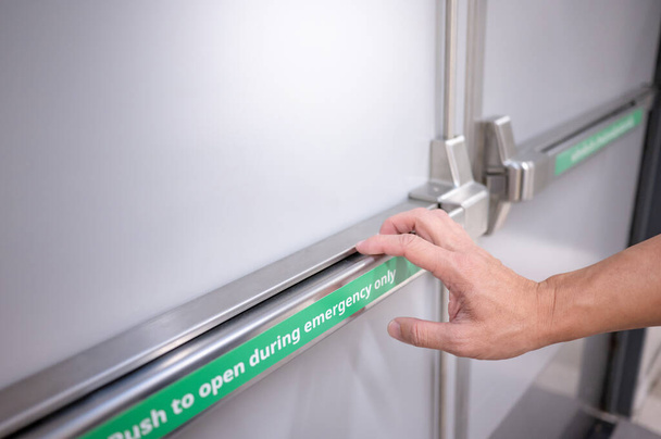 Male hand pushing stainless steel panic bar opening the emergency fire exit door in public building. Fire escape concept - Fotó, kép
