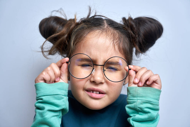 Caucasian little girl wearing glasses squinting while looking at camera isolated on white background. Vision problems concept - Foto, Imagem