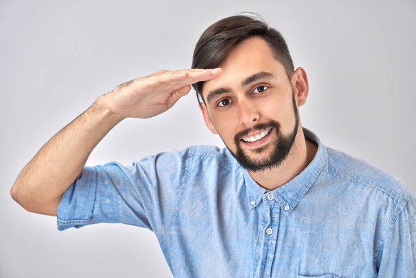 Caucasian young male in casual looks future, looking far away distance with hand over head isolated on white background. Search concept. - Foto, imagen