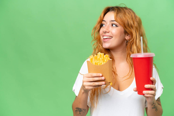 Young caucasian woman holding fried chips and soda isolated on green screen chroma key background  background - Фото, зображення