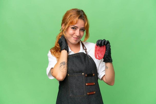 Boucher femme caucasienne portant un tablier et servir de la viande fraîche coupée isolée sur écran vert chroma arrière-plan clé rire - Photo, image