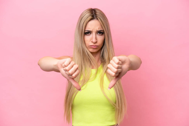 Pretty blonde woman isolated on pink background showing thumb down with two hands - Valokuva, kuva