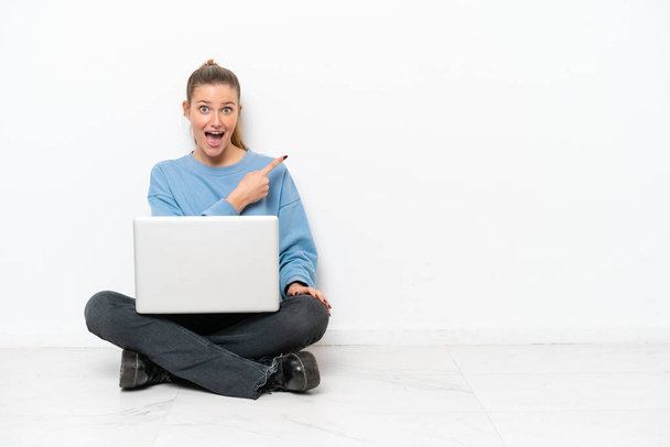 jonge vrouw met een laptop zitten op de vloer verrast en wijzen kant - Foto, afbeelding