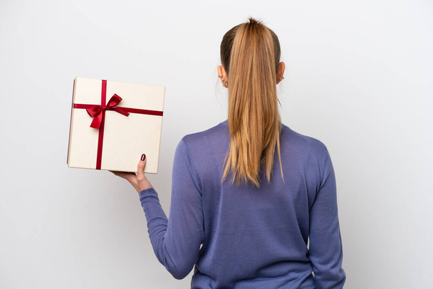 Young caucasian woman holding a gift isolated on white background in back position - Φωτογραφία, εικόνα