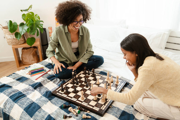 Щаслива американка і її дочка - підліток грають у шахи, сидячи вдома в ліжку. - Фото, зображення