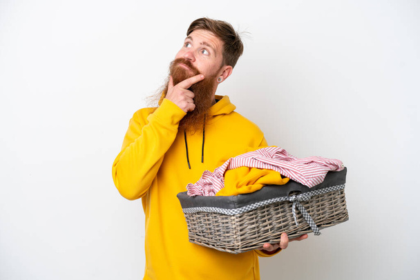 Redhead man with beard holding a clothes basket isolated on white background having doubts - Photo, Image